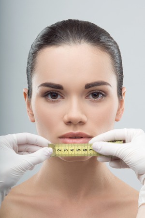 Woman face being measured by beautician hands, getting prepared for plastic surgery, isolated on greyの写真素材