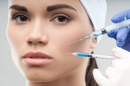 Closeup portrait of young Caucasian woman getting cosmetic injection of botox with two syringes, isolated over grey backgroundの写真素材