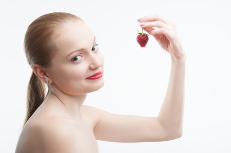 Waistup portrait of a young attractive smiling woman holding strawberry in hand, side view, isolated on whiteの写真素材
