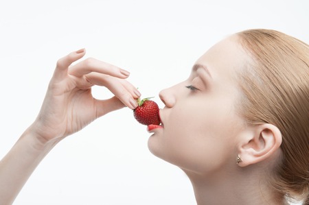 Closeup portrait of a young attractive woman eating strawberry, side view, isolated on whiteの写真素材