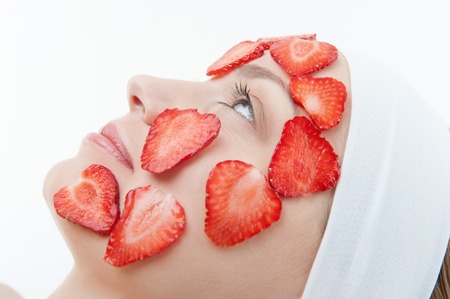 Beautiful young woman receiving facial mask of strawberry in beauty salon, side view closeup portrait isolated on whiteの写真素材