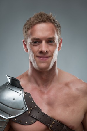 Closeup  portrait of young handsome muscular smiling man gladiator in armour posing  isolated over grey backgroundの写真素材