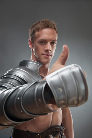 Half length portrait of young handsome muscular smiling man gladiator in armour showing ok sign with thumbs up, selective focus, isolated over grey backgroundの写真素材