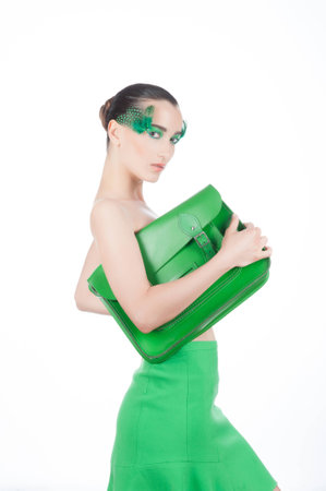 Beautiful brunette young woman with peacock style make-up and green satchel, green stylish garment, fashion model isolated on whiteの写真素材