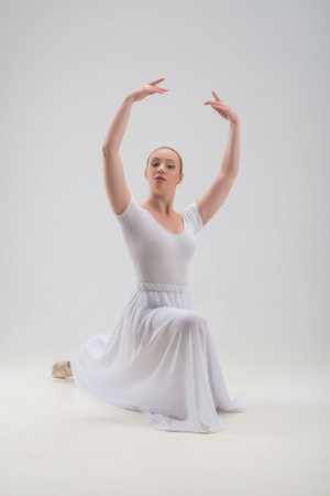 Full length portrait of young and beautiful modern style ballet dancer posing on knee isolated on white background, studio shotの写真素材