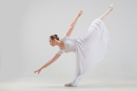 Full length portrait of young and beautiful modern style ballet dancer taking classical ballet poses, lifting leg up isolated on white background, studio shotの写真素材