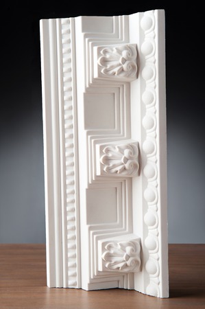 Fragment of white stucco molding, elements of decoration on wooden desk, closeup over dark...