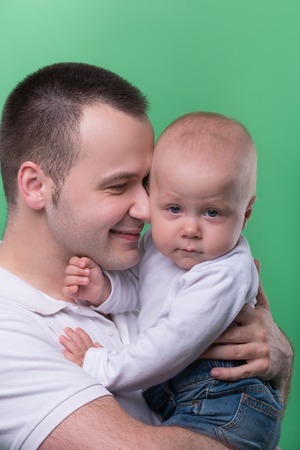 Closeup Portrait of happy smiling handsome father hugging and kissing his son baby boy in white polo shirt and jeans, family concept, isolated on green backgroundの写真素材