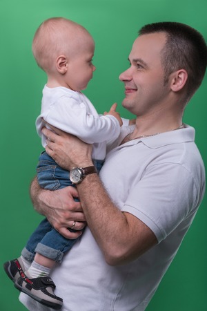 Half-length portrait of happy smiling handsome father embracing his son baby boy looking at each other, family concept, isolated on green backgroundの写真素材
