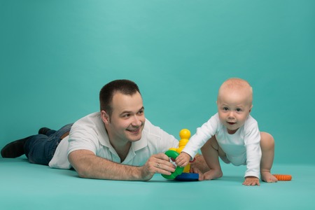 Happy handsome smiling Caucasian father playing with his son baby boy, picking up pyramid circles, isolated on blue  Family fun conceptの写真素材