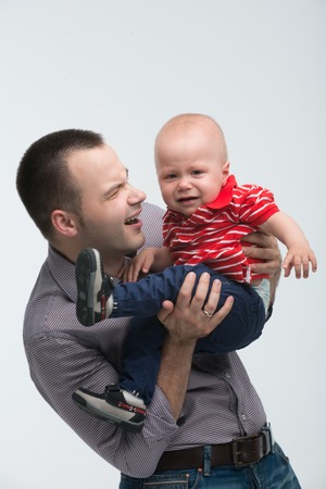 Portrait of young handsome Caucasian father holding her screaming toddler son being naughty and cranky, isolated on whiteの写真素材