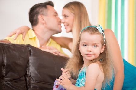 Closeup portrait of happy family, little cute daughter smiling while her parents caressing each other on background, home interiorの写真素材