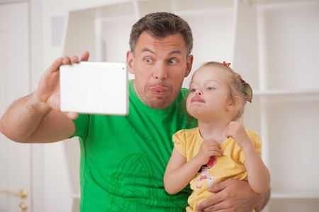 Closeup portrait of happy smiling father and child using electronic tablet at home making selfie, having fun and playing foolの写真素材