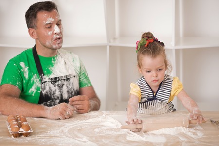 Half-length portrait of cute little daughter with handsome father cooking pastry, working with rolling pin  Dirty apronsの写真素材