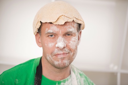 Closeup portrait of Funny handsome man with dough on his head  Upset cook in apron with flour on his face on white backgroundの写真素材