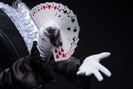 Half-length portrait of  juggler wearing interesting black costume and white shirt showing us his cards  Isolated on black backgroundの写真素材