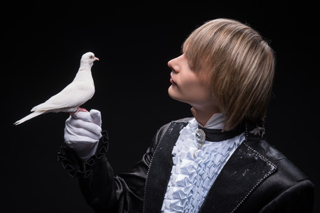 Half-length portrait of fair-haired matchless juggler wearing interesting black costume and white shirt holding pouter on his hand thinking about the next trick  Isolated on black backgroundの写真素材