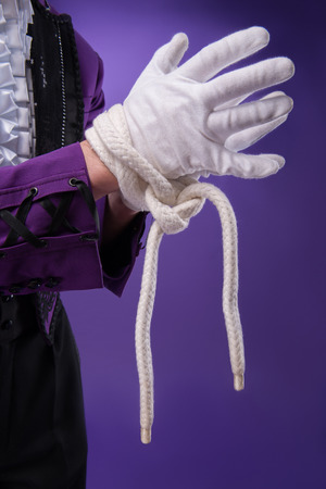 Half-length portrait of juggler wearing splendid violet jacket white shirt and black pants standing aside with tied hands in white gloves  Isolated on blue backgroundの写真素材