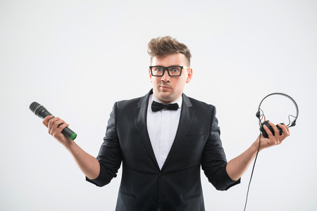Half-length portrait of stylish emotional DJ in tuxedo posing with microphone and headphones isolated on white backgroundの写真素材