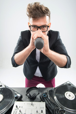 Top view portrait of stylish emotional DJ in tuxedo posing with microphone by turntable isolated on white backgroundの写真素材