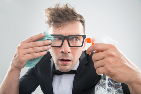 Funny half-length portrait of stylish hipster man in tuxedo and bowtie in spectacles cleaning his...