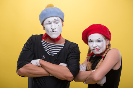 Close-up horizontal portrait of couple of two funny mimes holding their hands on their chest isolated on yellow background with copy placeの写真素材