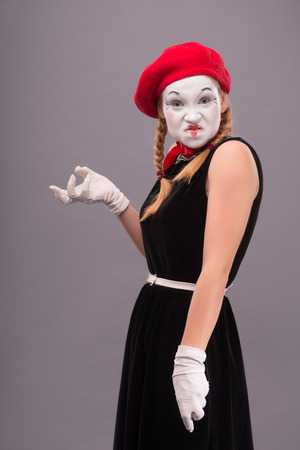 Waist-up portrait of angry female mime in red head and with white face showing with her hands horror isolated on grey background with copy placeの写真素材