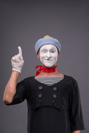 Waist-up portrait of male mime with grey hat and white face funny showing sign Attention isolated on grey background with copy placeの写真素材