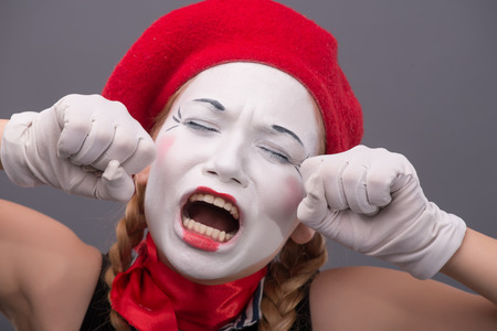 Close-up portrait of young mime girl yawning, closing her eyes and showing with her hands that she wants to sleep, isolated on grey background with copy placeの写真素材