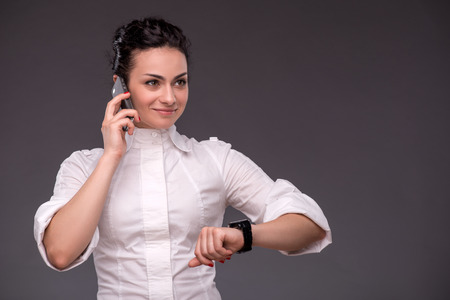 Waist-up portrait of successful businesswoman talking per telephone and looking at the watches and ahead with confidence and smileの写真素材