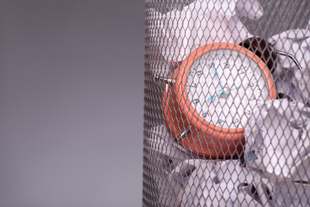 Close-up photo of a clock in refuse bin with other office rubbish like documents and papersの写真素材