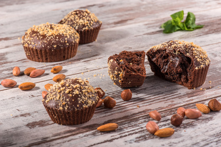 Close-up picture of four chocolate cupcakes one of them broken decorated with almonds, hazelnut and mint on wooden table in cafe with copy placeの写真素材