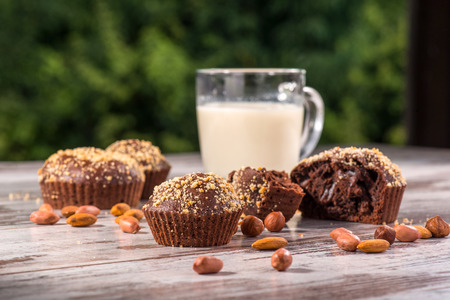 Close-up picture cup of milk and four chocolate cupcakes one of them broken decorated with almonds and hazelnut on wooden table in cafe with copy placeの写真素材