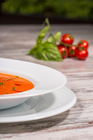Close-up picture of cold tasty tomato soup gazpacho with species on the wooden table in vegan cafe with tomatoes standing near a plate, with copy place and selective focus on a half of the plateの写真素材