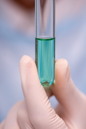 Close-up picture of a tube with some green substance in hands of female scientist in laboratory while doing some experiments isolated on blue backgroundの写真素材