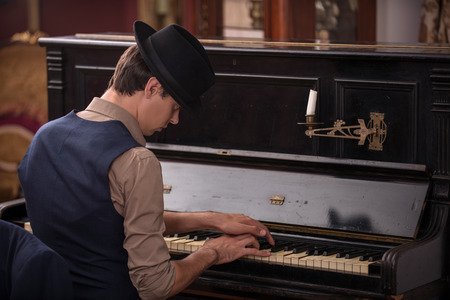 Waist-up portrait of a musician in suit and in black hat playing the piano with the feelings in baroque interior sitting back to the cameraの写真素材