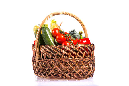 Lovely basket with fresh vegetables including pepper lettuce tomatoes corn broccoli and cucumber is pleasure for every vegetarian. Isolated on white backgroundの写真素材