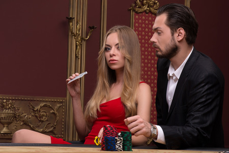 beautiful woman in casino holding in hand  cards and  handsome man looking at her  sitting at table waist upの写真素材