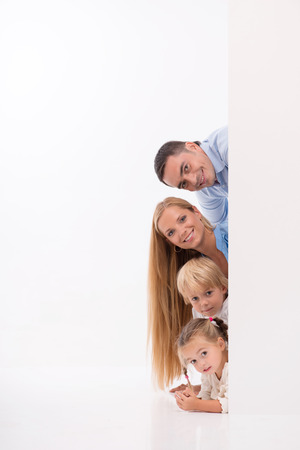 Happy family of father mother son and daughter smiling  looking  out wall  isolated on white background with copy placeの写真素材
