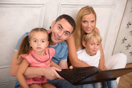 Happy family of father mother son and daughter smiling  looking  at camera sitting by notebook   isolated on white background with copy place top viewの写真素材