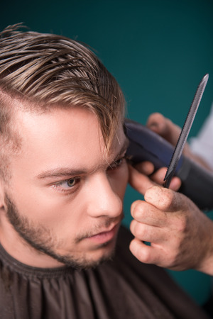 hairdresser  cuts    hair  with hair clipper on back of the head of handsome satisfied  client in  professional  hairdressing salon top viewの写真素材