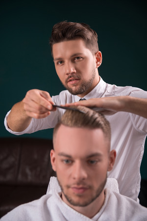 hairdresser  does   hair  with black comb of handsome satisfied  client in  professional  hairdressing salonの写真素材