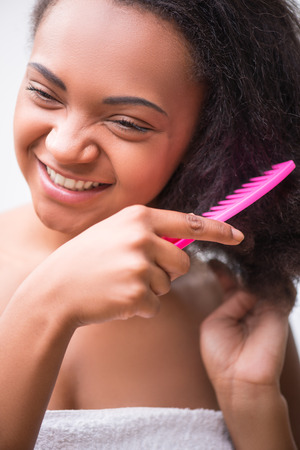 Beautiful  dark skinned girl combing her hair with rose comb  isolated on white background smiling looking asideの写真素材