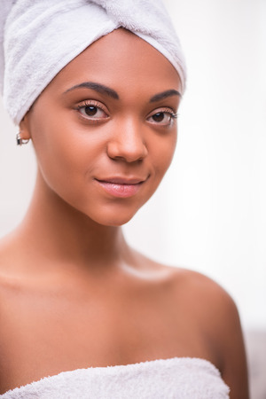 Portrait of beautiful  dark skinned girl in white towel on head and body  looking at camera isolated on white backgroundの写真素材