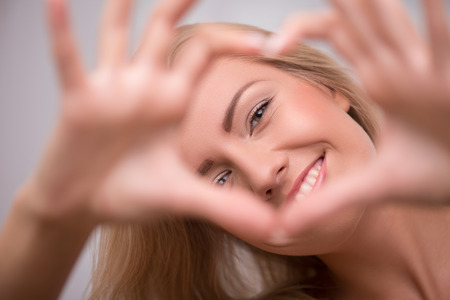Portrait of beautiful happy fun blond girl in white  T shirt  looking at camera smiling showing heart with her hand and fingers    selective focus close upの写真素材