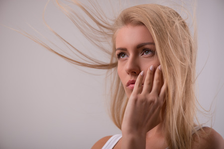 Portrait of beautiful thoughtful disappointed blond girl in white  T shirt  looking aside with  flying  hair    with copy placeの写真素材