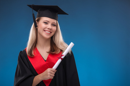 Portrait of beautiful happy blond girl in black cloak and master hat holding bundle of sheet of...