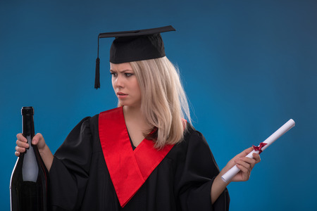 Portrait of beautiful disappointed  blond girl in black cloak and master hat thinking her wish holding bundle of sheet of paper and bottle on blue backgroundの写真素材