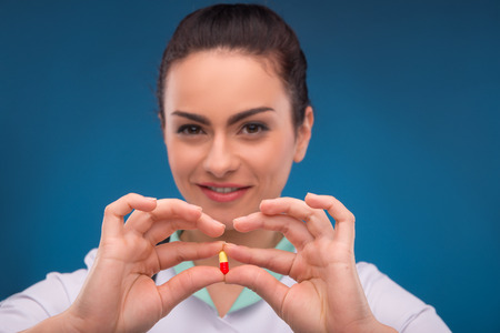 Portrait of beautiful woman doctor on blue background with stethoscope smiling looking at camera holding with fingers red white tabletの写真素材