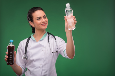 Portrait of beautiful happy  woman doctor with stethoscope showing preference to   bottle of mineral  water waist upの写真素材